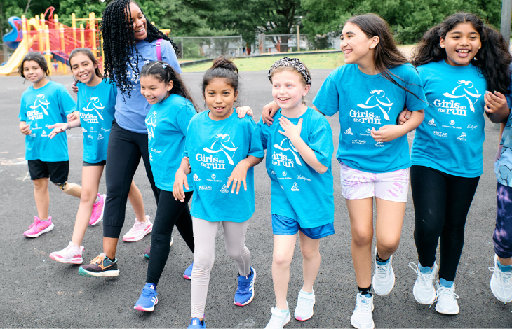 Image of seven Girls on the Run teammates and coach in a line with arms linked and smiling at the camera